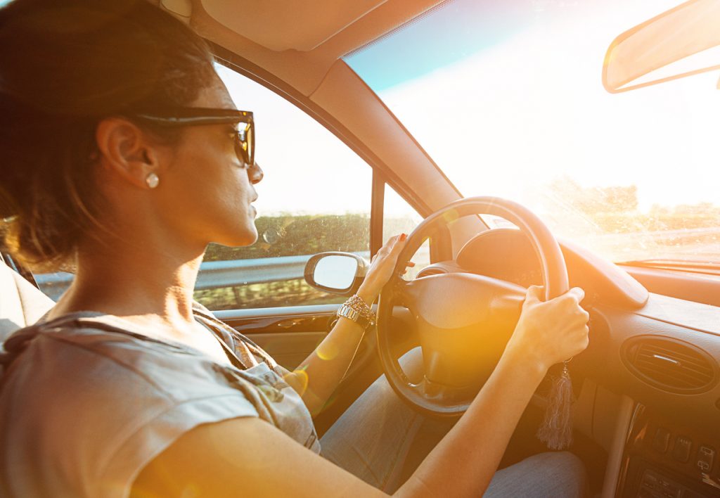 Casual woman driving a car on highway and looking into rear view mirror.